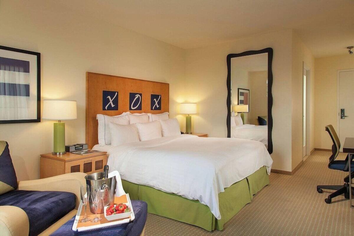 A hotel room with a large bed, bedside lamps, a nightstand, a chair, a desk, and a mirror.