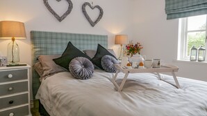 A neatly made bed with a tray of tea and cups, a bedside table with a lamp, and two heart-shaped wall decorations.