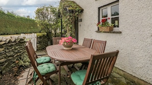 An outdoor wooden table with four chairs, a potted plant, and a stone wall.