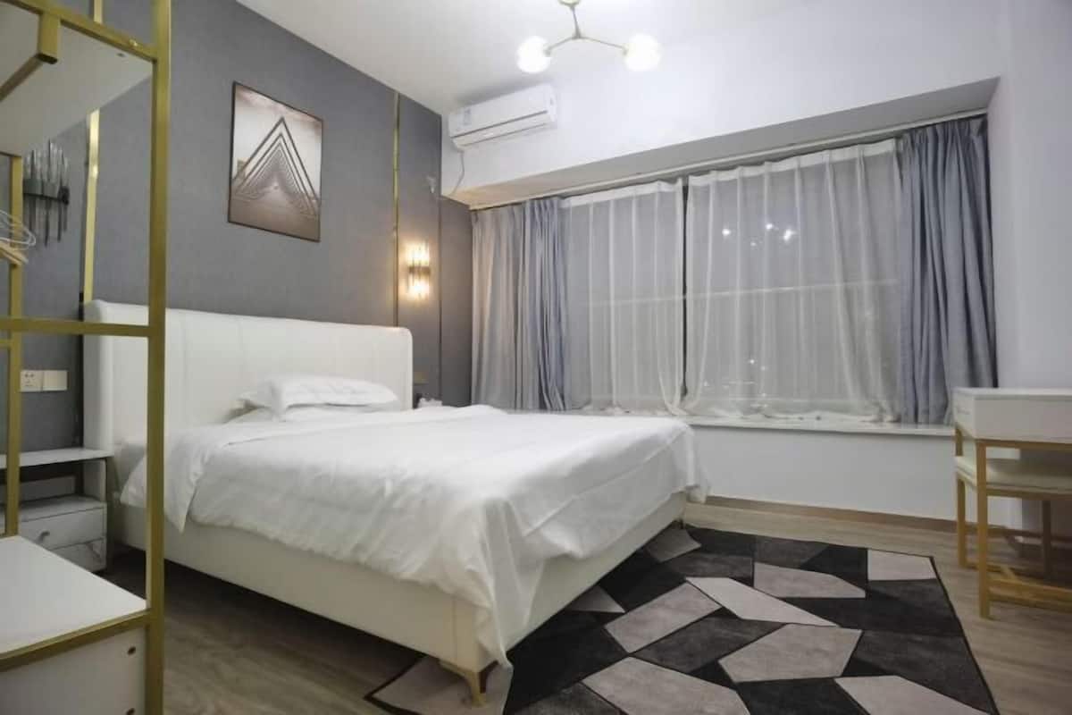 Une chambre à coucher avec un lit, une fenêtre avec des rideaux, une table de chevet et un climatiseur fixé au mur.