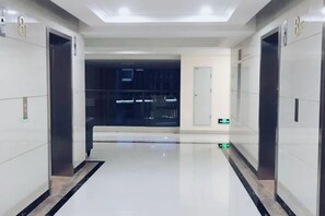 A modern elevator area with a clean, polished floor and walls, and a visible emergency exit door. - Youshang International Apartment (Guangzhou Huadu Sunac Tourism City Branch) (Guangzhou)