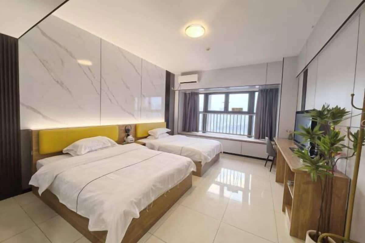 Une chambre d’hôtel avec deux lits, un bureau en bois, une télévision et une fenêtre avec des rideaux.