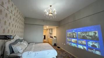 Habitación de hotel con cama, candelabro y una pantalla mural que muestra escenas de cine.