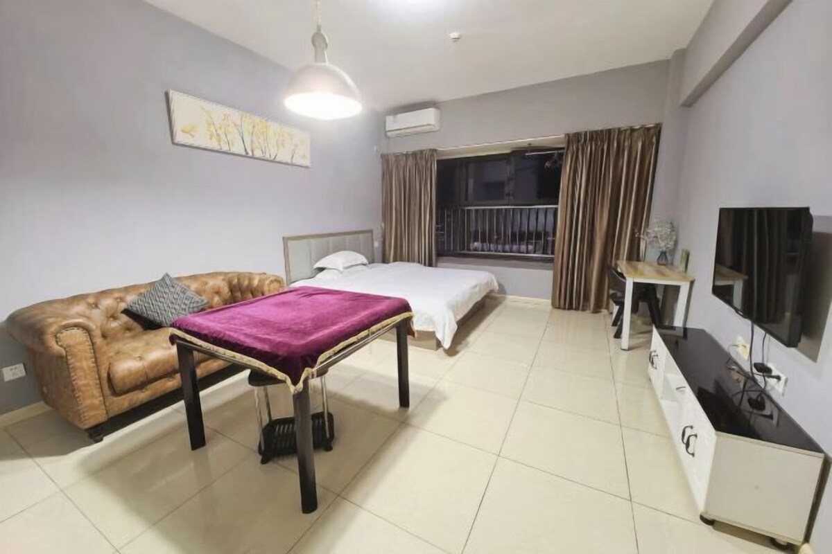 A hotel room with a bed, a sofa, a small table, a TV, and a window with curtains.