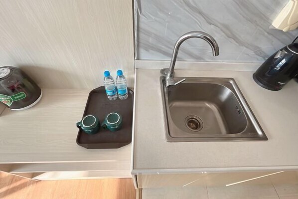A modern kitchen with a stainless steel sink, a tray with two water bottles and two green cups, and a coffee maker on the counter. - Youshang International Apartment (Guangzhou Huadu Sunac Tourism City Branch) (Guangzhou)