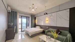 Une chambre d’hôtel moderne avec un lit, un canapé vert, une table basse blanche et une vue sur l’extérieur, visible à travers une porte vitrée.