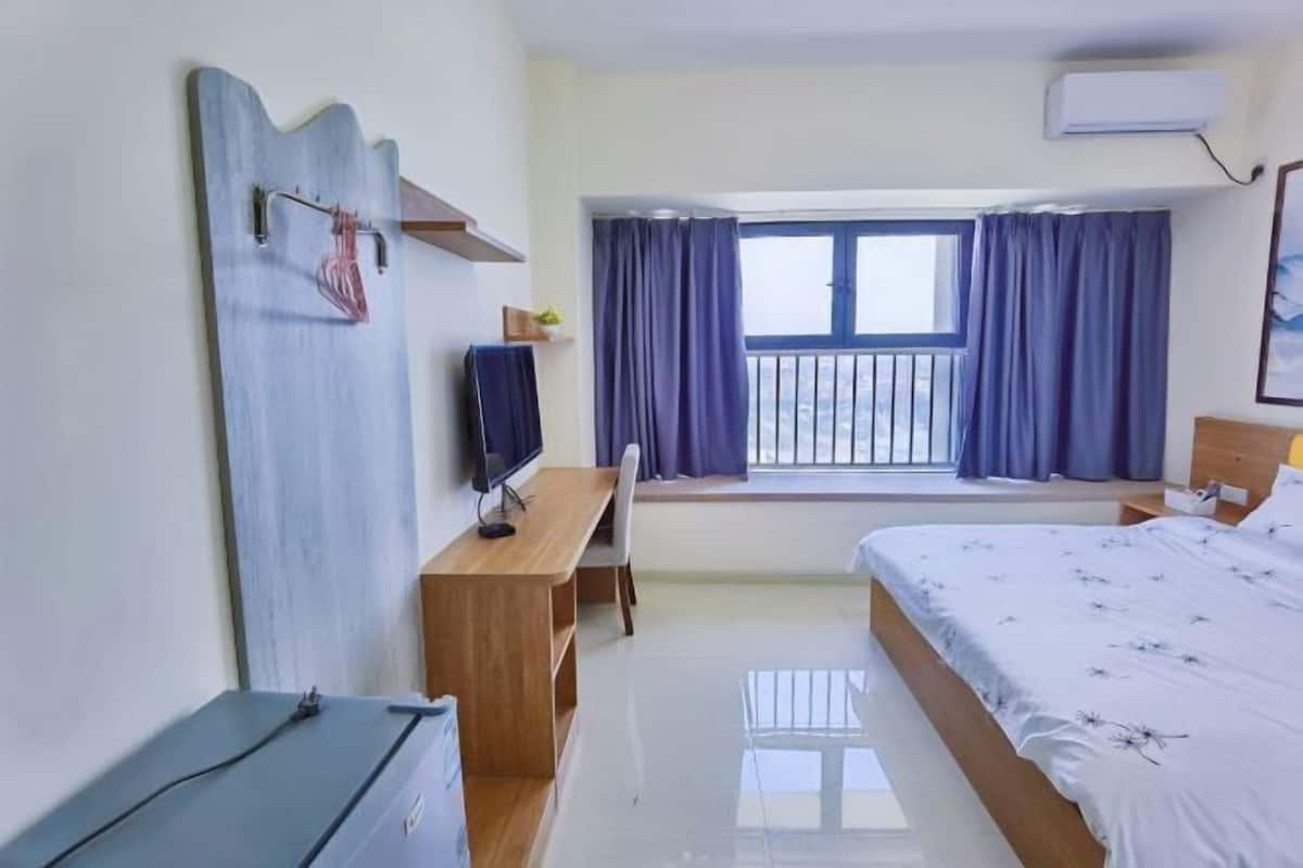 Une chambre d’hôtel avec un lit, un bureau, une chaise, une télévision et une fenêtre avec des rideaux.