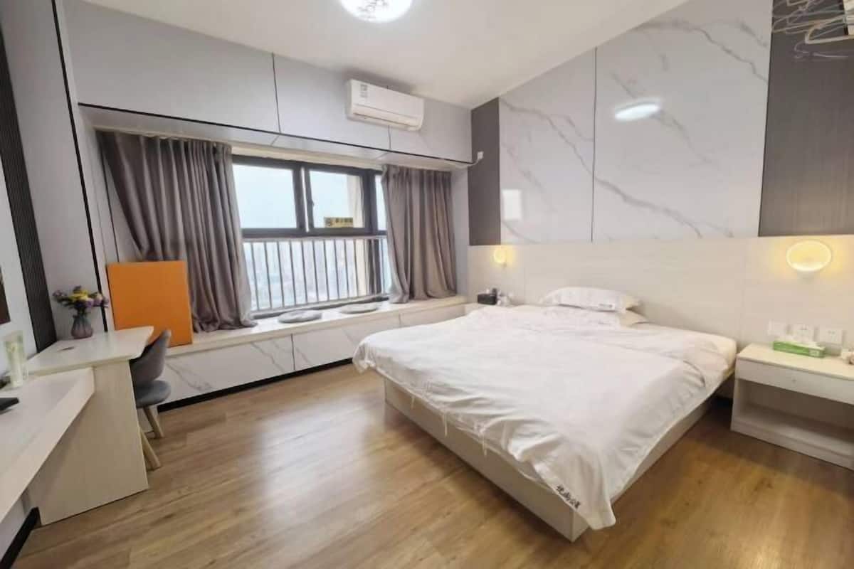 Une chambre d’hôtel moderne équipée d’un lit, de tables de chevet, d’un bureau, d’une fenêtre avec des rideaux et de panneaux muraux en marbre.
