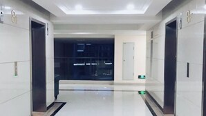 Un hall d’ascenseur moderne, doté d’un sol épuré et réfléchissant, et d’une porte en verre donnant sur un espace faiblement éclairé.