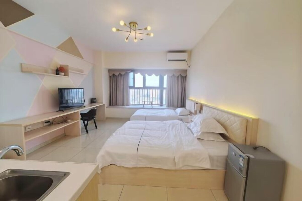 A hotel room with two beds, a desk with a chair, a television, a refrigerator, and a window with curtains.