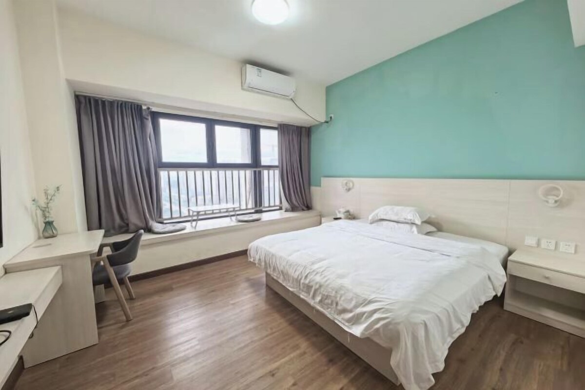 A bedroom with a bed, a desk, and a window with curtains.