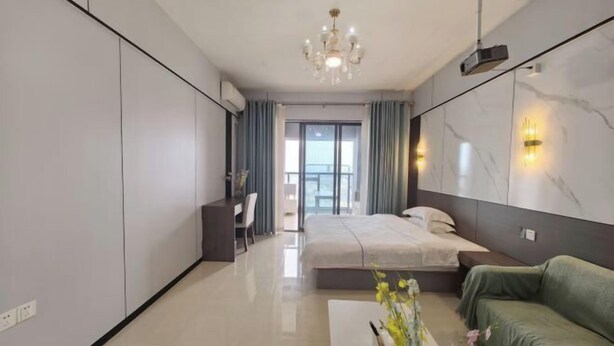 Une chambre d’hôtel moderne avec un lit, un canapé vert, un bureau et un lustre.