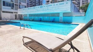A swimming pool with lounge chairs, a diving board, and a building in the background.