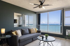 Ein modernes Wohnzimmer mit einem grauen Sofa, einem runden Couchtisch und einem Deckenventilator.