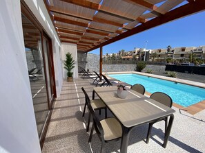 A poolside area with a covered patio, outdoor seating, and a view of the pool.