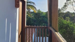 A wooden balcony with a view of lush greenery and a clear sky.