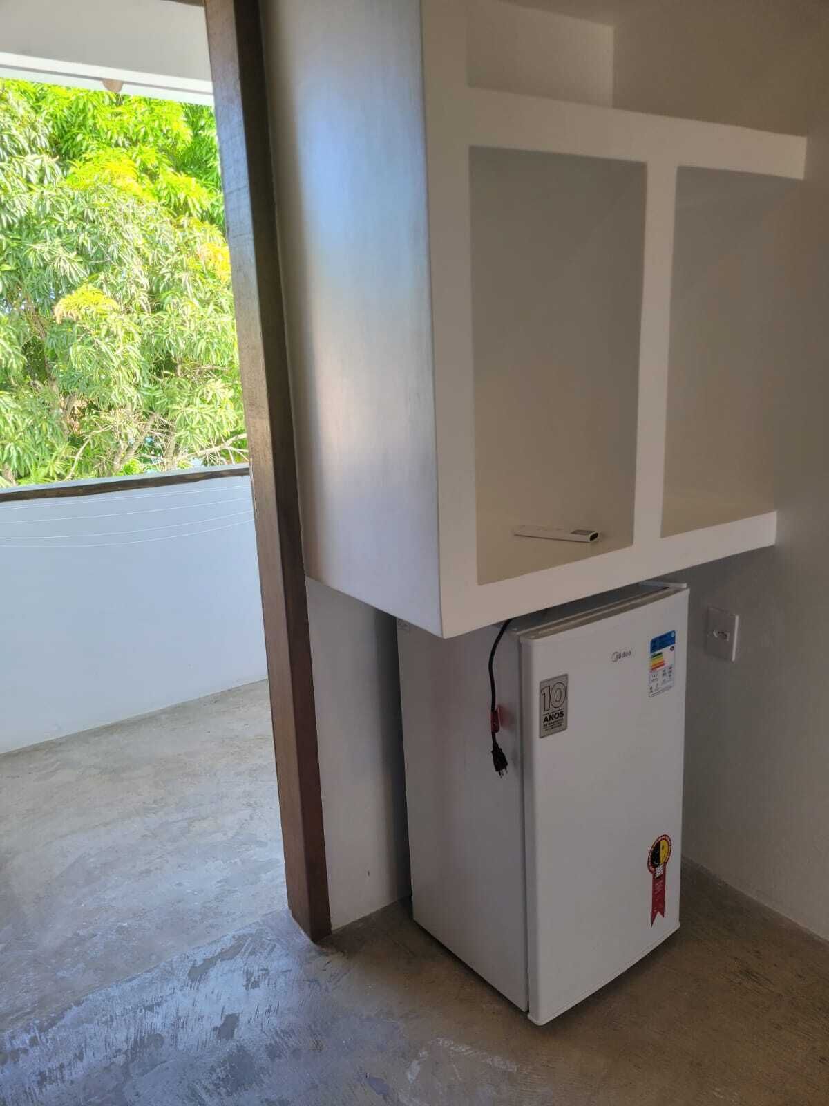 A compact room with a small white refrigerator, a cabinet above it, and a concrete floor.