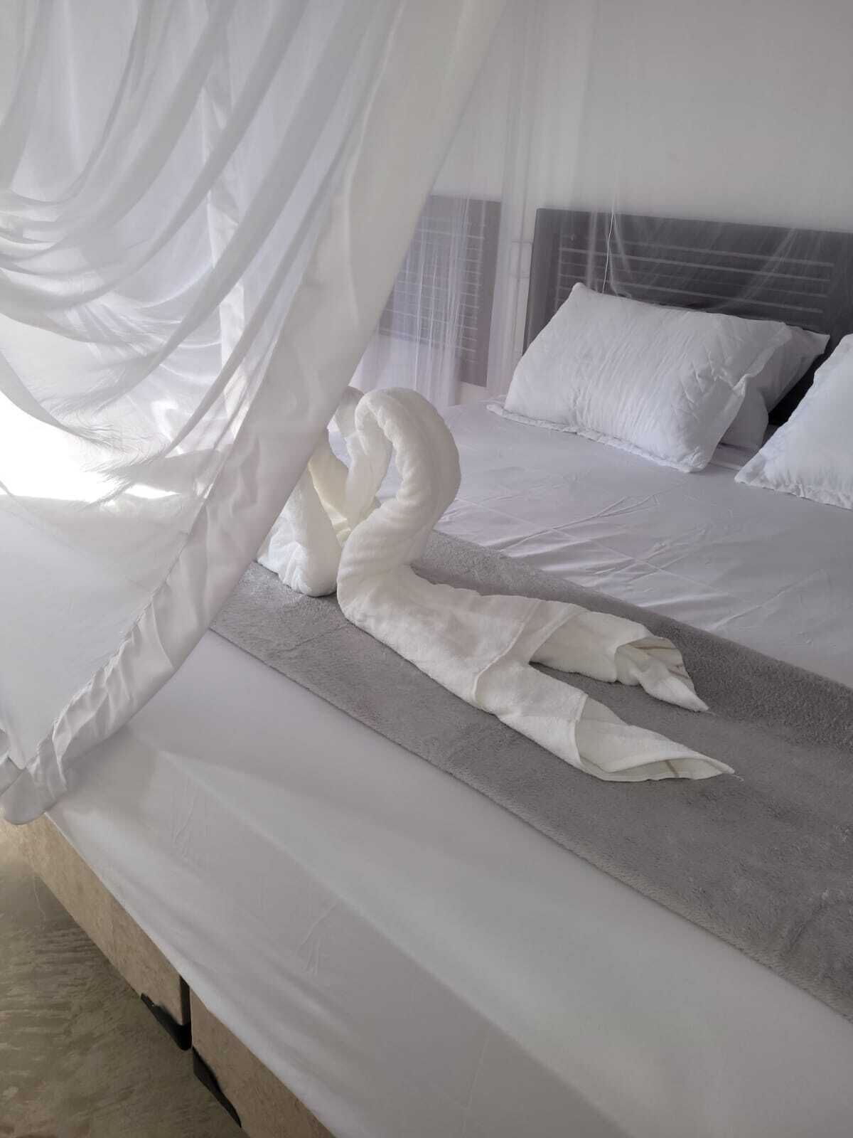 A bed with white linens, a grey mattress, and a canopy with a swan-shaped decoration.