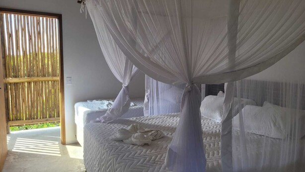 A bedroom with a bed covered in white bedding, a canopy, and a view of a wooden fence through a window.