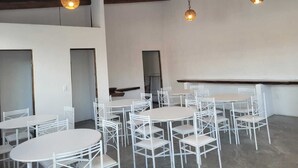 A spacious room with multiple round tables and white chairs, a high wooden ceiling, and hanging woven light fixtures.