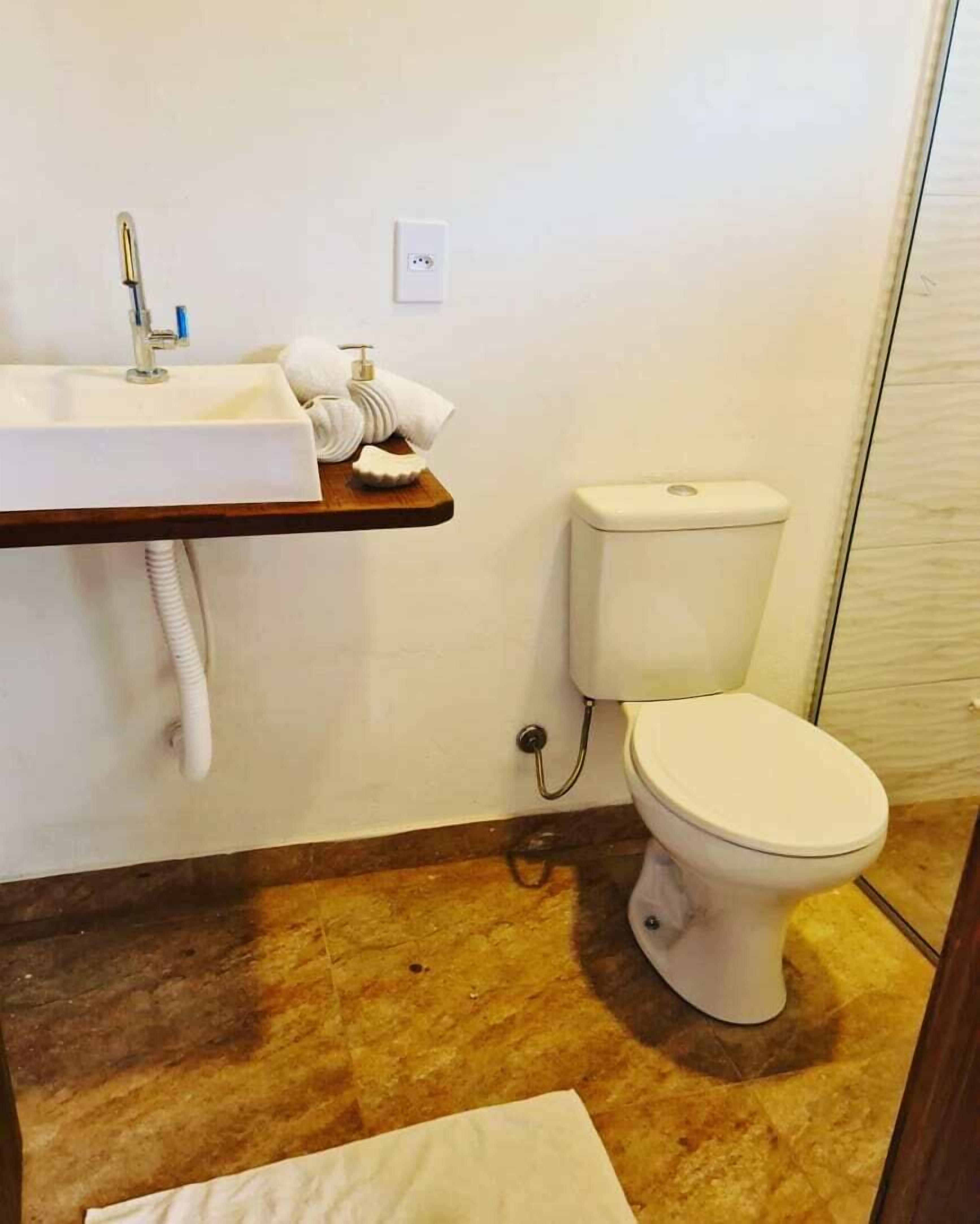 Een badkamer met een wit wastafelmeubel, toilet en een houten plank.