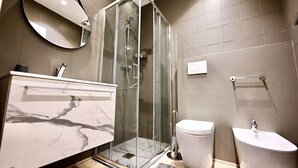 Ein modernes Badezimmer mit einer gläsernen Duschkabine, einem Marmorwaschtisch, einer Toilette und einem Bidet.