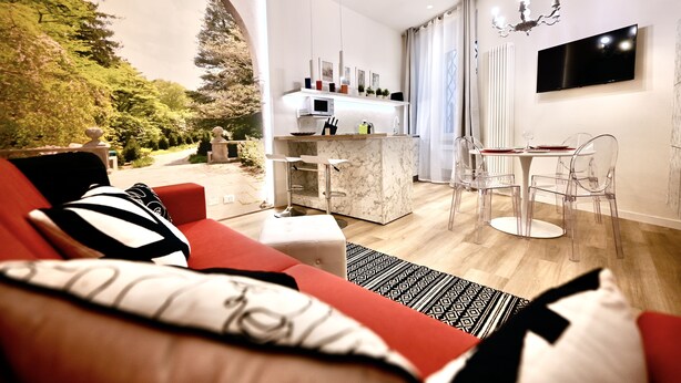 Ein modernes Wohnzimmer mit einem roten Sofa, einem Marmor-Couchtisch und einem Essbereich mit transparenten Stühlen.