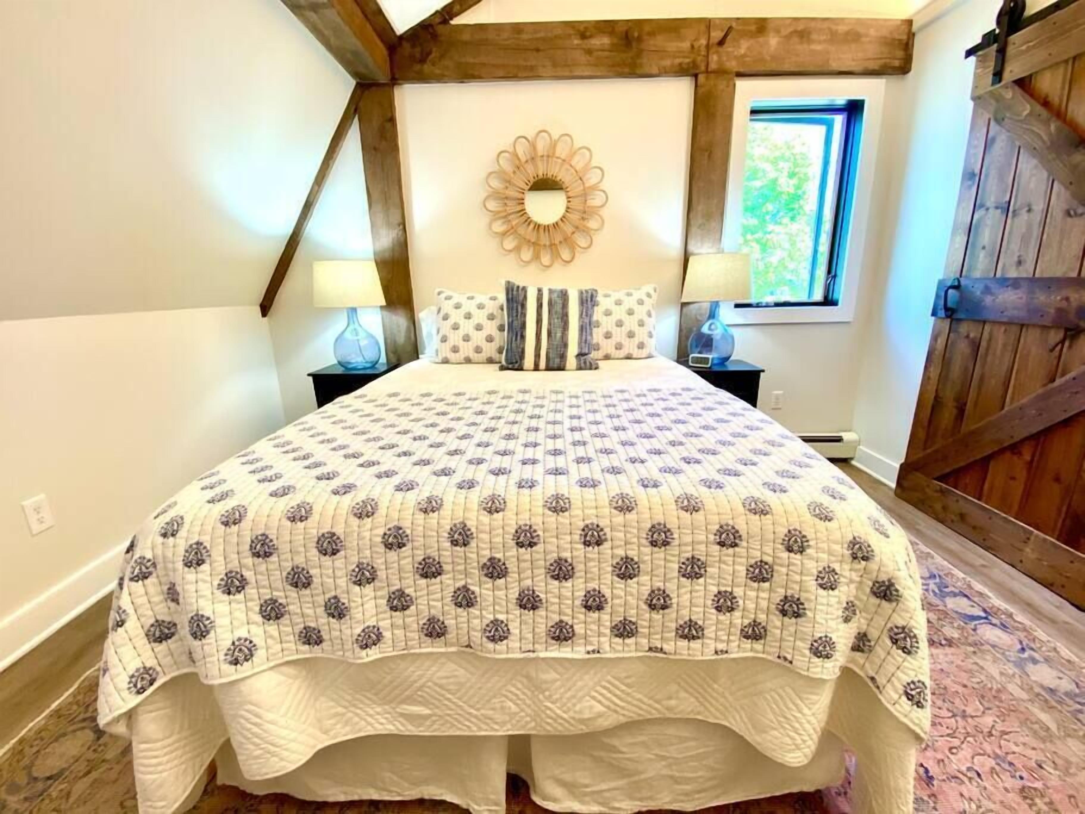 A bedroom with a large bed, a decorative mirror, and a window with a view of greenery.