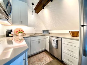 Une cuisine moderne avec des armoires blanches, un réfrigérateur en acier inoxydable, une machine à café, un grille-pain et un saladier en bois posé sur le comptoir.