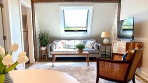En hyggelig stue med sofa, sofabord, et sengebord med lampe, fjernsyn og en lænestol.