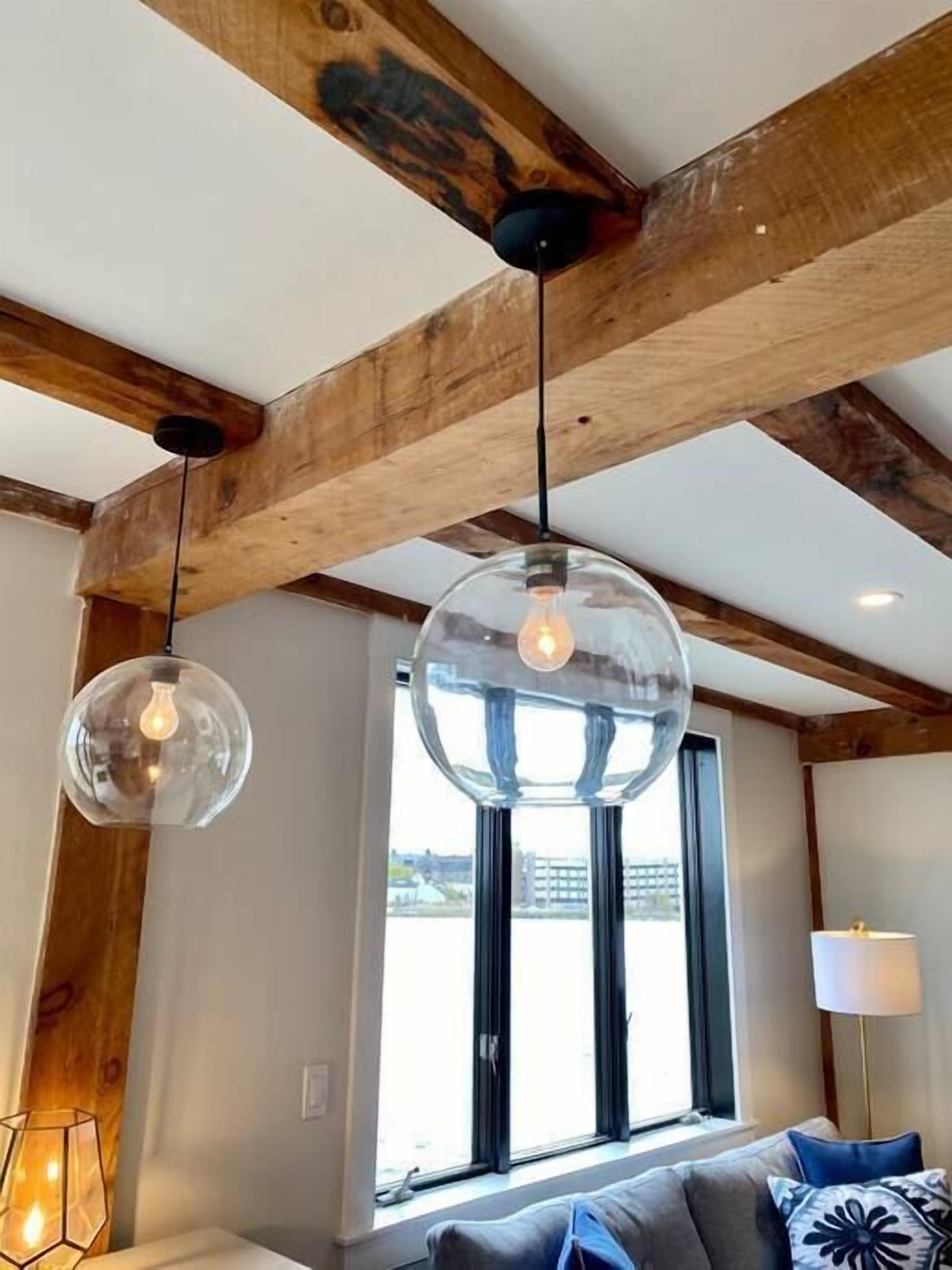A room with a wooden ceiling, a large window, and a bed with pillows.