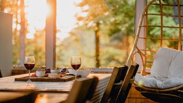 Une table à manger avec des verres à vin, des bols d’olives et de fromage, et une chaise en osier.