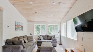 Un salon moderne avec un canapé gris, un banc en bois et un téléviseur à écran plat fixé au mur.