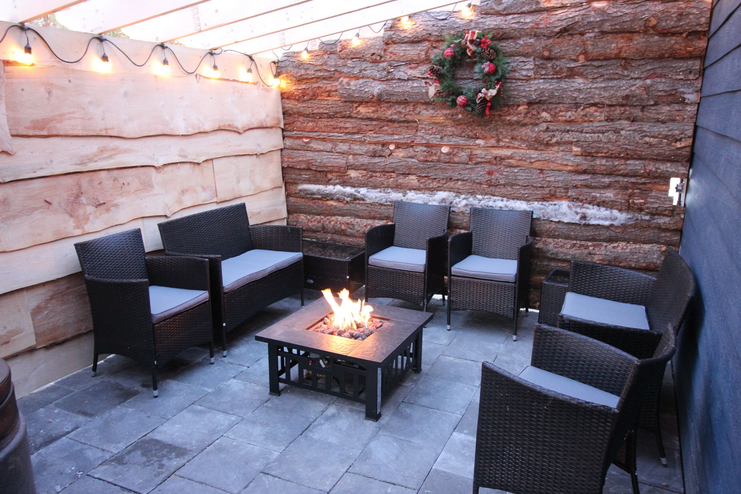 An outdoor patio with wicker furniture and a central fire feature.