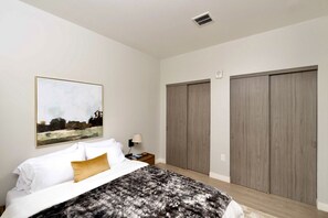 A bedroom with a bed, a nightstand, a lamp, a painting, and two wardrobes. - Walker`s Point Apt with Gym and Balcony | Sleeps 4-5 (Milwaukee)