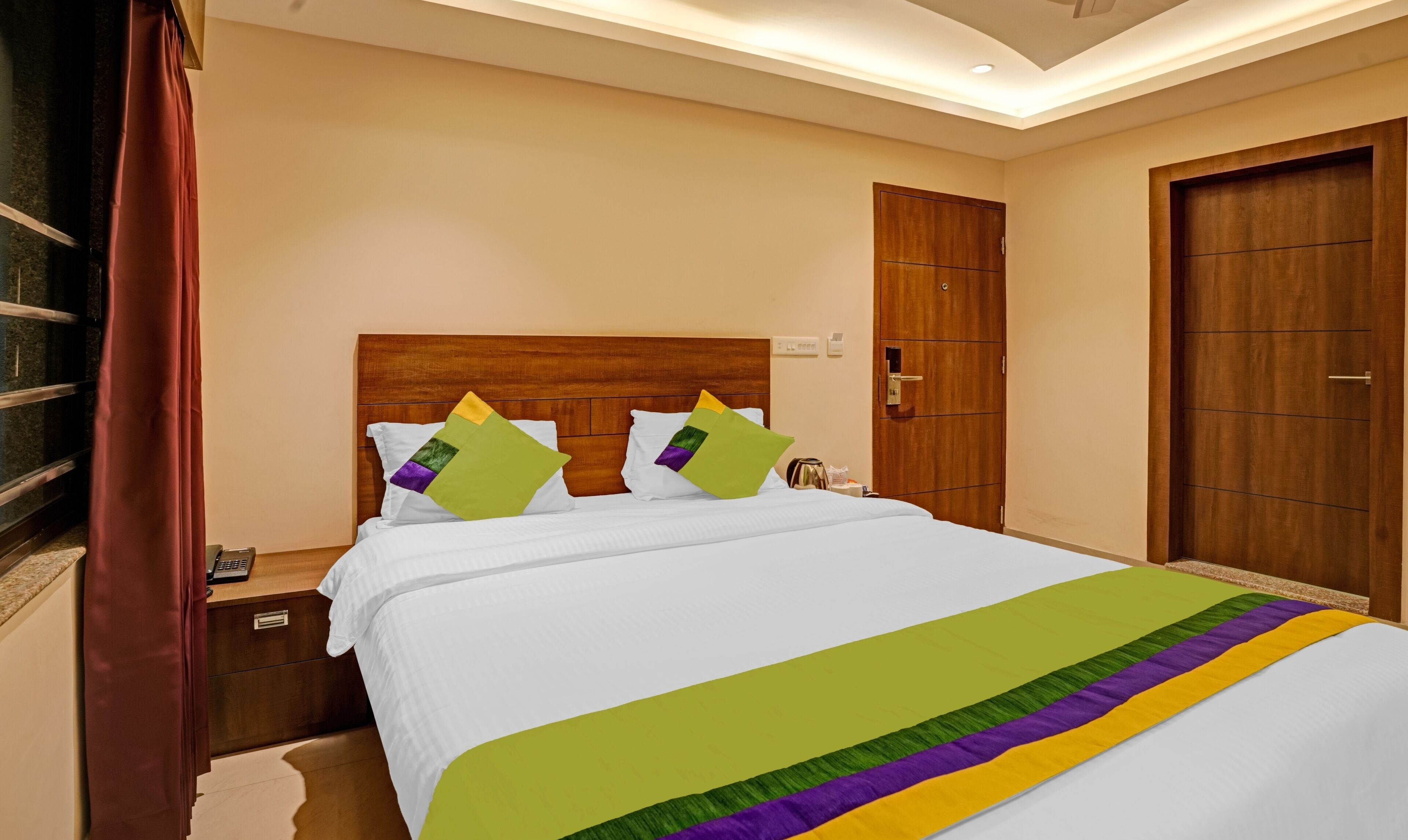 Una habitación de hotel con cabecera de madera, cama con ropa blanca, dos almohadas, mesita de noche y una puerta.