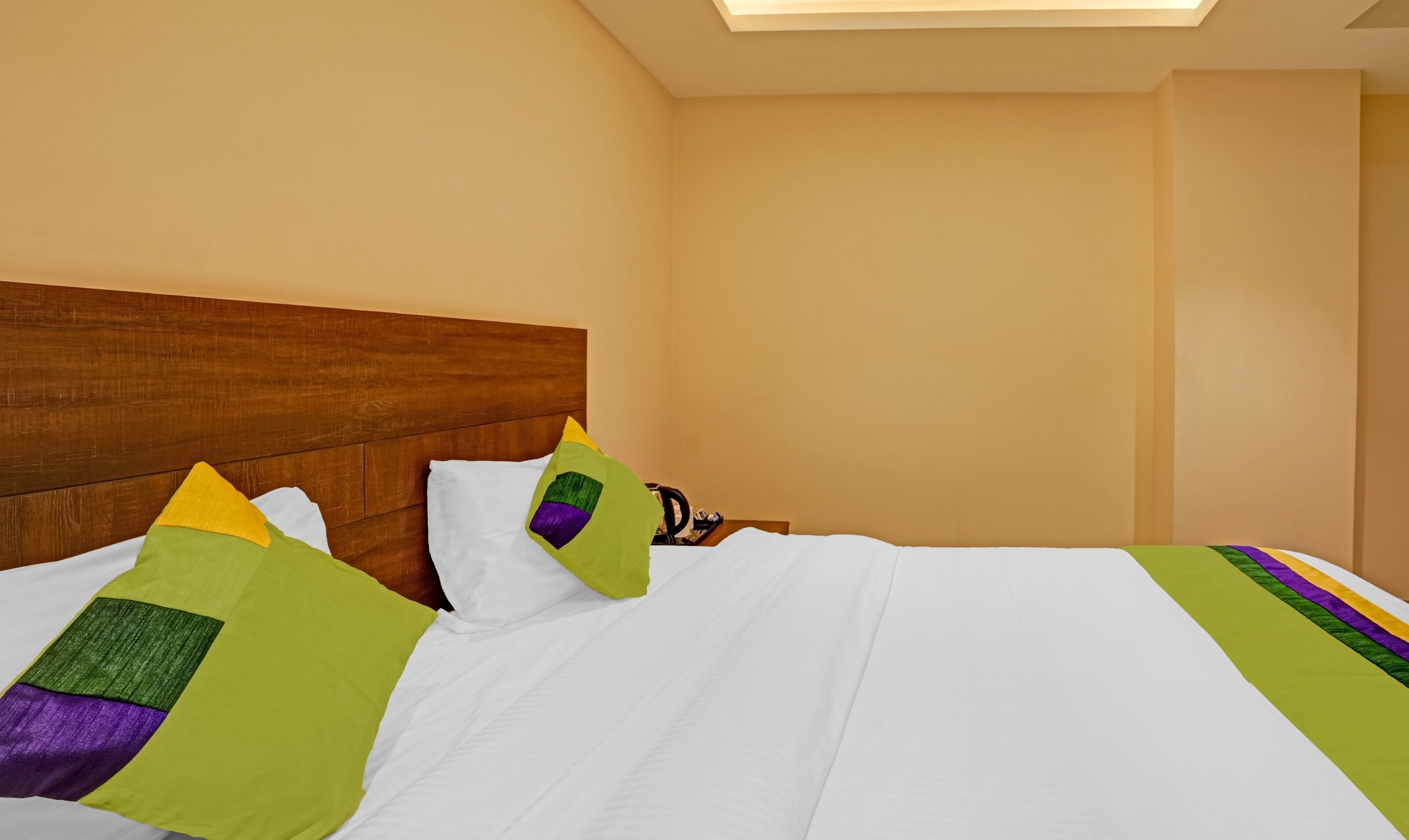 Una habitación de hotel con cabecera de madera, cama con ropa de cama blanca y almohadas de colores.