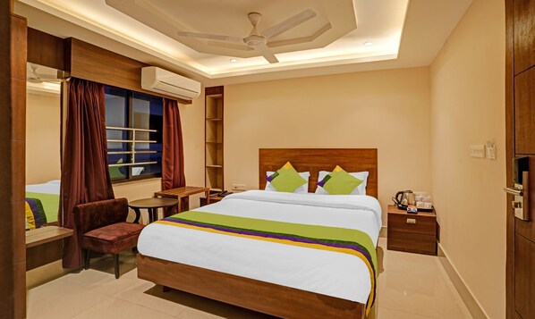 Une chambre d’hôtel avec un grand lit, un bureau, une chaise, une armoire et un ventilateur de plafond.