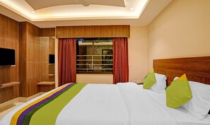 Une chambre d’hôtel moderne avec un grand lit, des murs recouverts de panneaux de bois, un téléviseur fixé au mur et une fenêtre avec des rideaux rouges.
