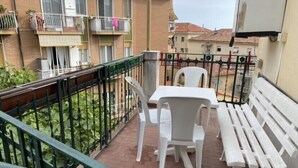 A balcony with a white plastic table and chairs, a white bench, and a metal railing. - Apartment (Imperia)