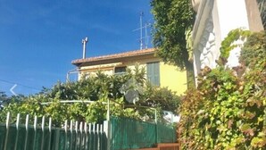 A yellow building with a tiled roof, surrounded by greenery and a green fence. - Apartment (Imperia)