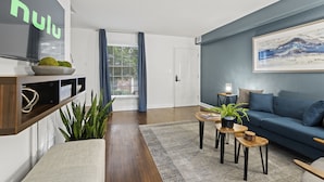 A modern living room with a blue sofa, a coffee table, and a bookshelf. - Cozy Condo * Office* Near Luxury Mall & Uptown (Charlotte)