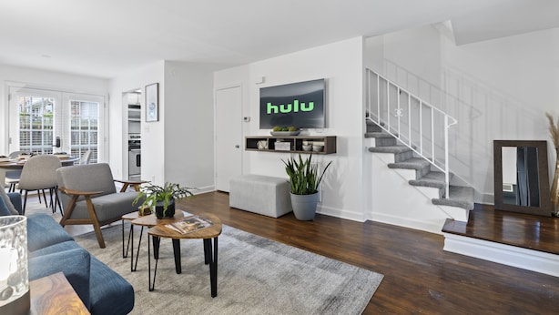 A modern living room with a large flat-screen TV, a staircase, and a dining area. - Cozy Condo * Office* Near Luxury Mall & Uptown (Charlotte)