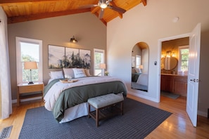 A bedroom with a bed, bedside lamps, a bench, a large window, and a mirror.