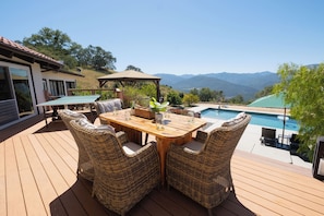 A wooden deck with wicker furniture, a pool, and a mountain view.