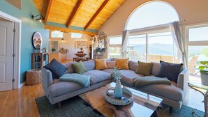 A cozy living room with a wooden ceiling, a large window with a view, a gray sofa, and a coffee table. - Mountain Retreat, Pool+Great Views, 30 days (Carmel Valley)