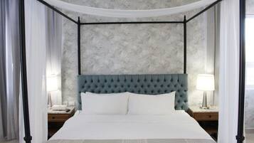 Una cama con dosel y cuatro columnas, un cabecero capitonado, dos mesitas de noche con lámparas y un estampado de papel tapiz floral.