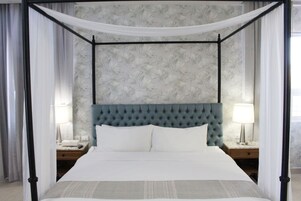 Una cama con dosel y cuatro columnas, un cabecero capitonado, dos mesitas de noche con lámparas y un estampado de papel tapiz floral.