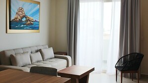 Een moderne woonkamer met een bank, een eettafel en een stoel. Er hangt een schilderij aan de muur en er is een raam met gordijnen.