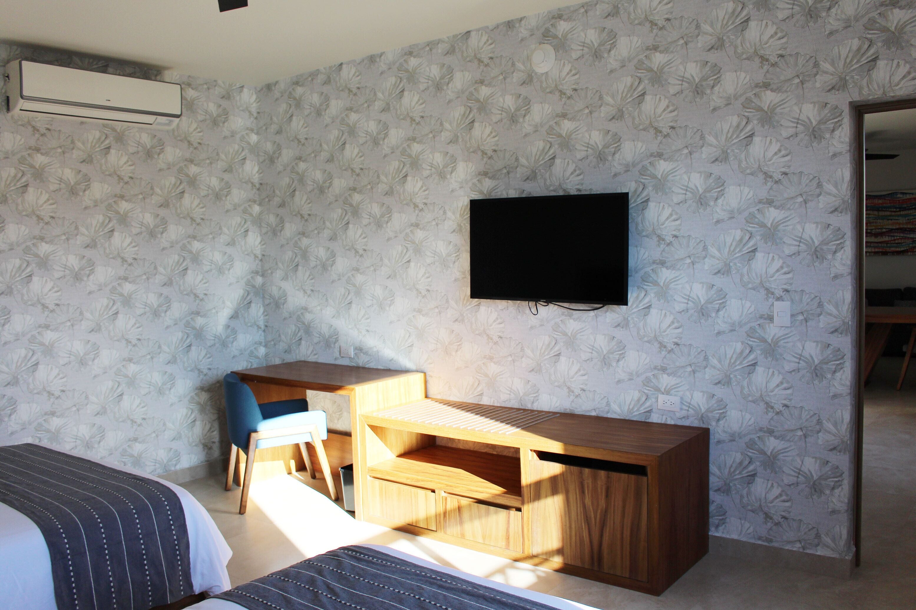 Une chambre d’hôtel avec un lit, un bureau, une chaise et un téléviseur fixé au mur.